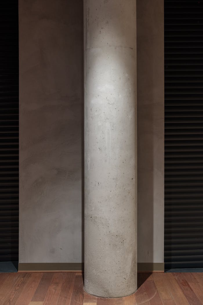 Concrete column in a minimalist room with wooden flooring and subtle lighting.