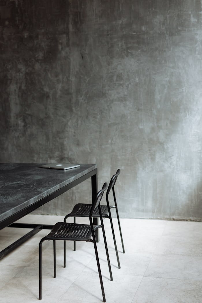 services-01 Elegant minimalist interior with marble table and metal chairs against a concrete wall.